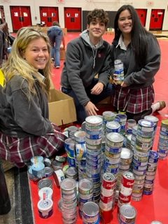 Seniors Avery Whitlow, Mark Pritchard and Alleana de Leon packing canned meats for the Thanksgiving food drive on the gym floor (Charli Esposito).
