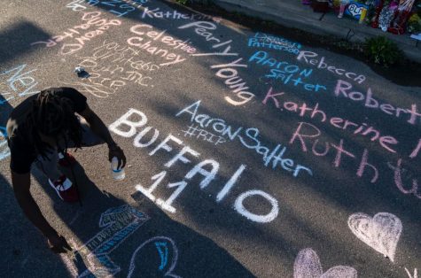Aaron Jordan adds to a sidewalk chalk mural depicting the names of the people killed at a mass shooting at Tops Friendly Market in Buffalo, NY on Sunday, May 15, 2022. (Photo courtesy of Kent Nishimura / Los Angeles Times via Getty Images)