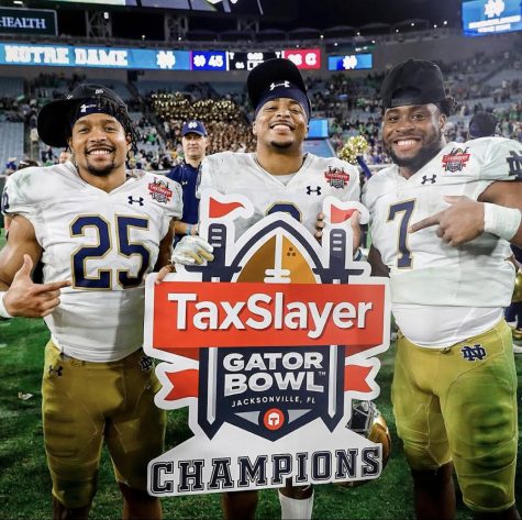 Notre Dame running backs (left to right) Chris Tyree, Logan Diggs and Audric Estimé hold “Taxslayer Gator Bowl Champions” sign. (Photo courtesy of Irish Sports Daily)