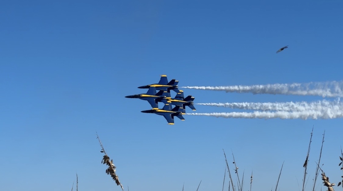 Four out of the six Blue Angel jets fly by in a compact formation.