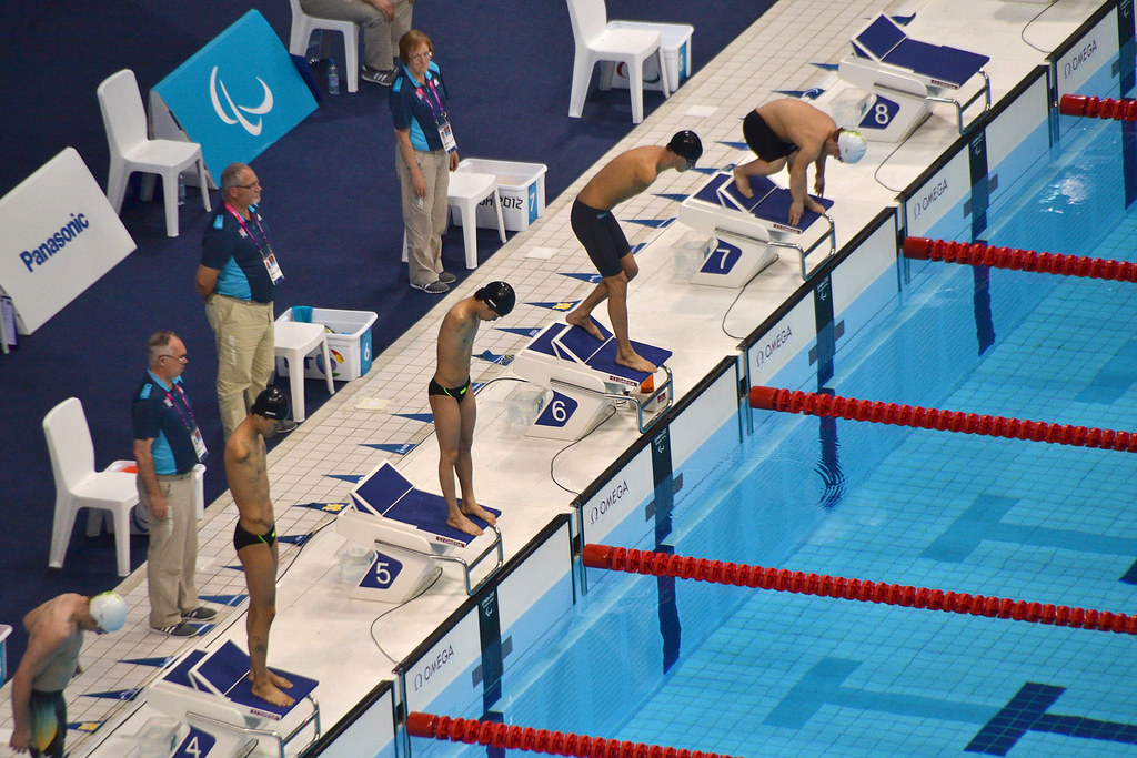 Swimmers in the Men's 50 meter butterfly step up onto the diving block. 